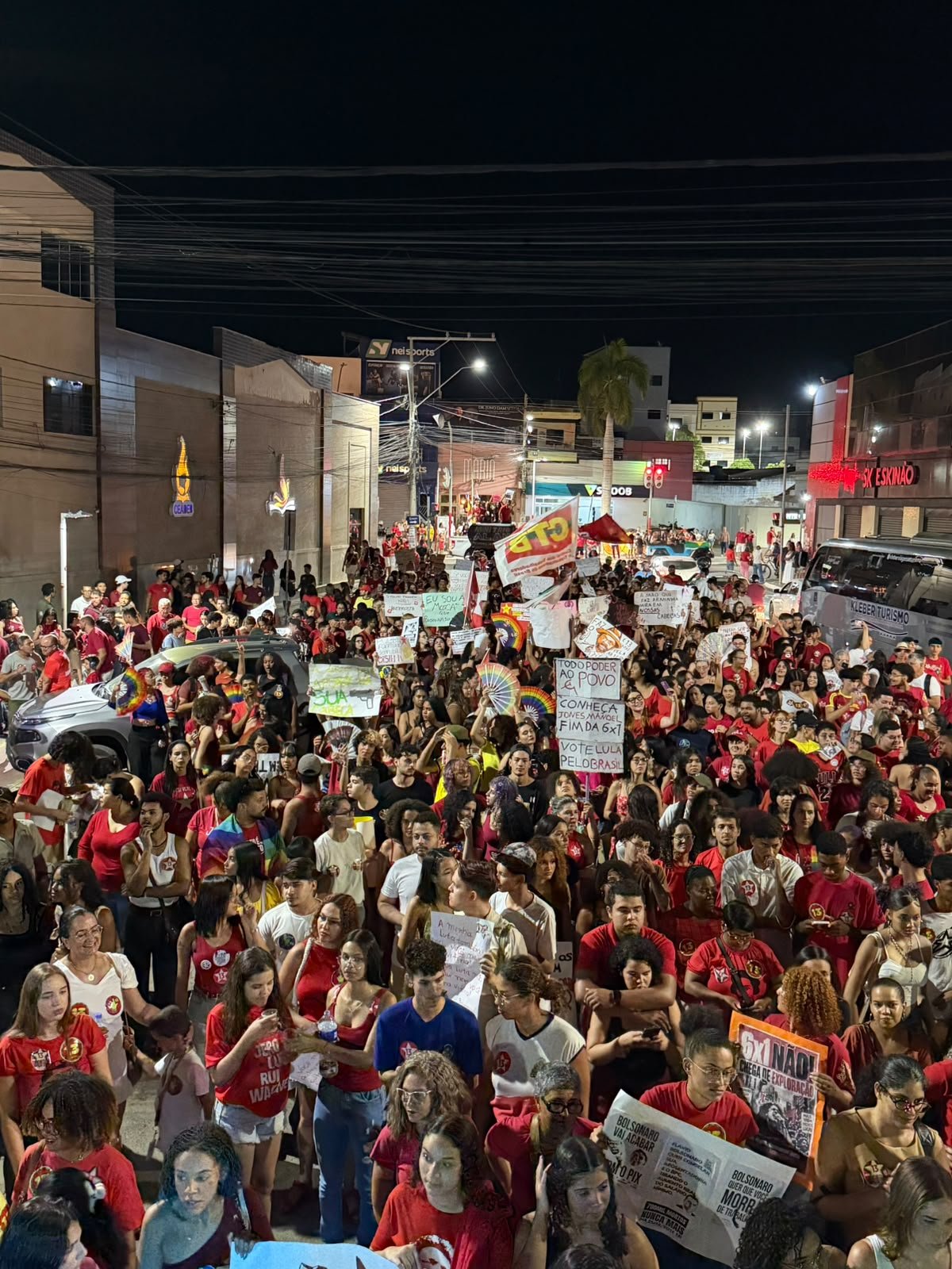 Fotografia em plano aberto mostrando a caminhada de manifestantes, estudantes e trabalhadores com faixas e bandeiras pelas ruas do centro de Irecê.