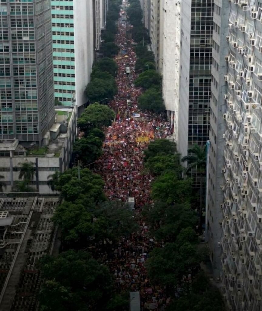 Multidão de jovens e apoiadores políticos reunidos em praça pública, segurando bandeiras e faixas durante manifestação de apoio à candidatura de Lula no segundo turno das eleições.