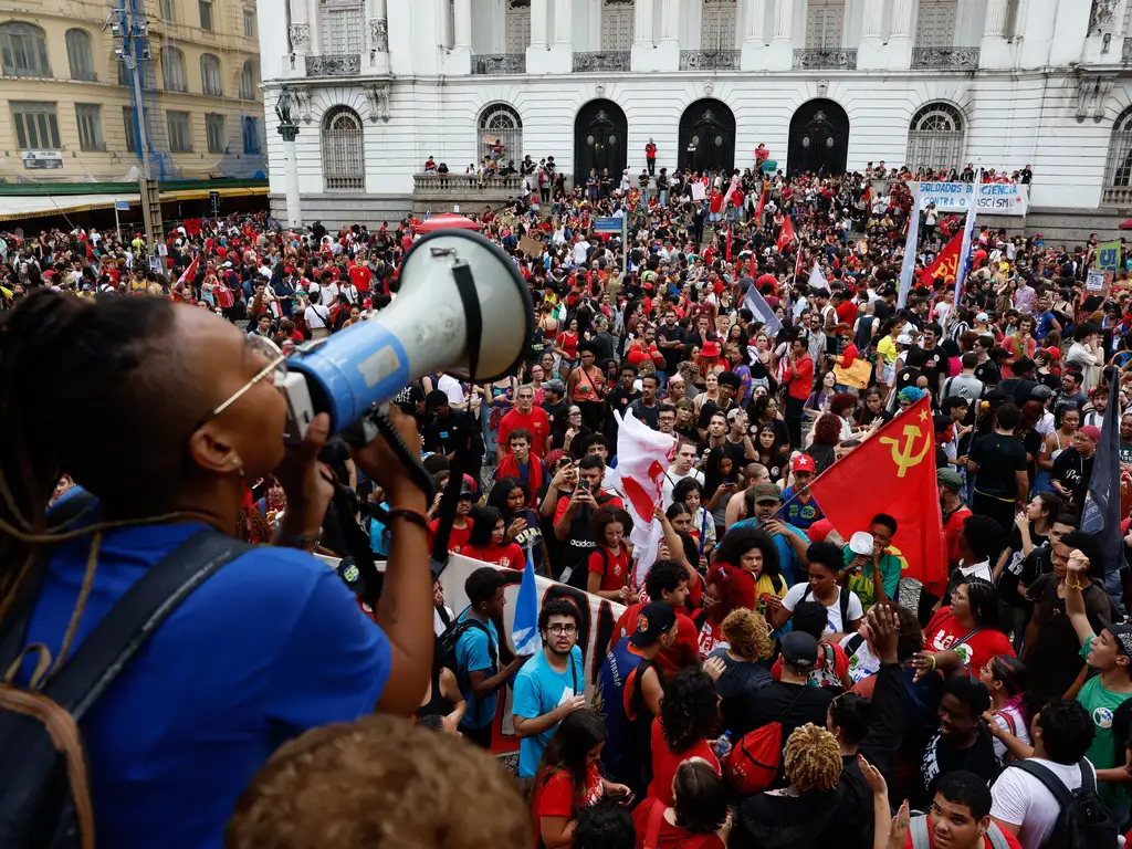 Multidão de manifestantes e estudantes reunidos em passeata segurando bandeiras e faixas durante ato de mobilização política nas ruas.